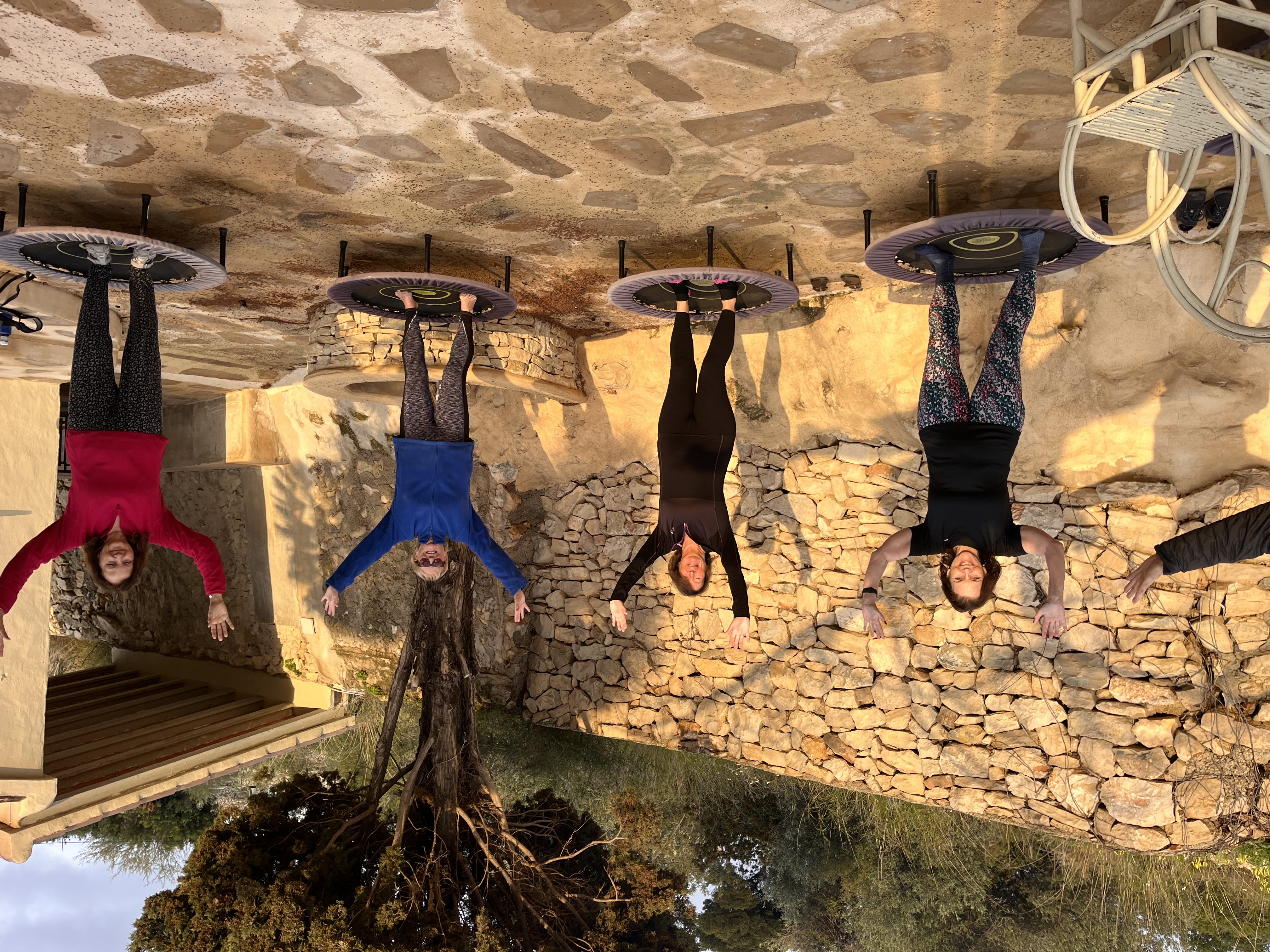 Four women upside down on mini-trampolines outdoors.