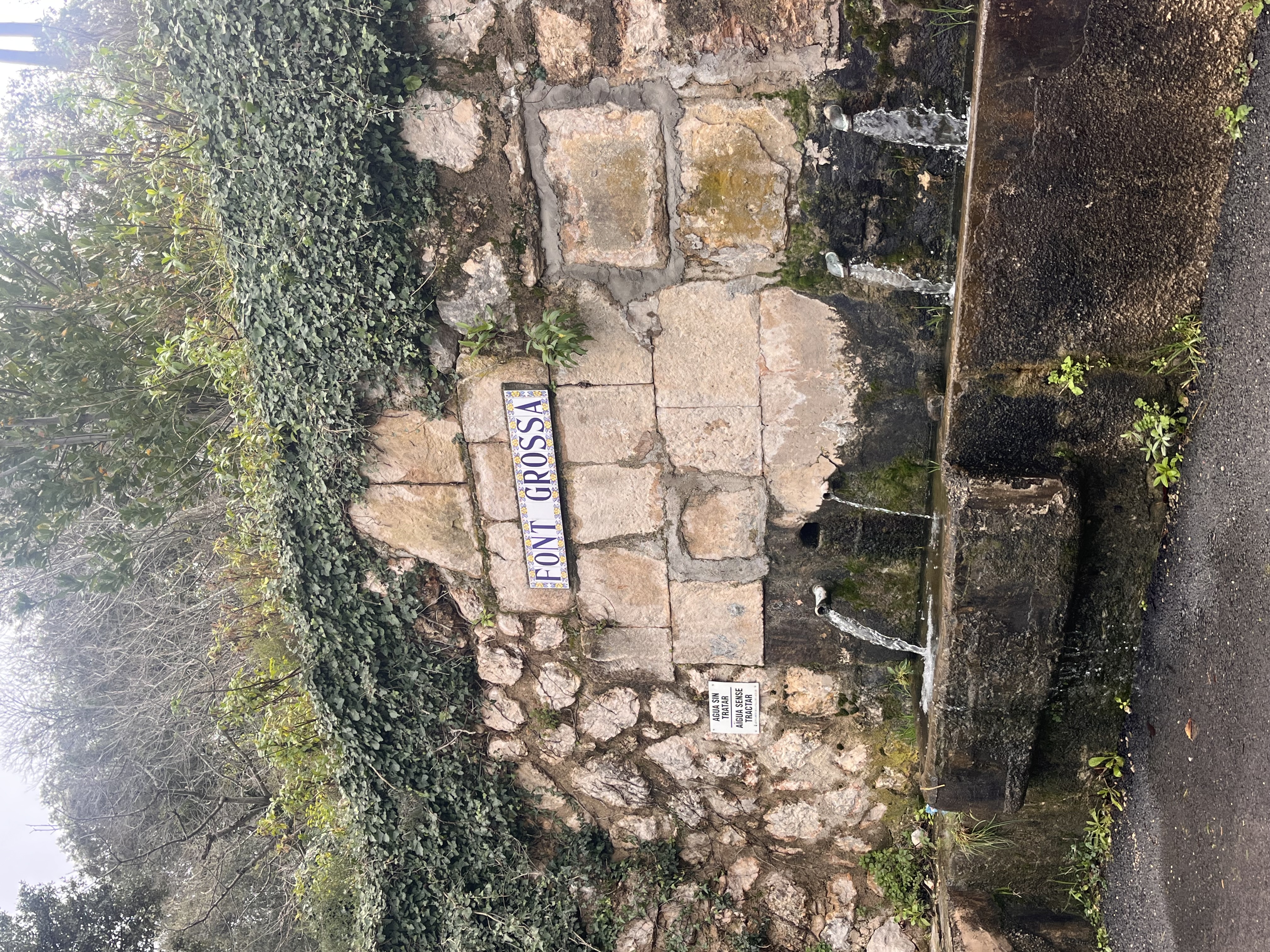 Rustic stone wall with water spouts and Font Grossa sign in Spain.